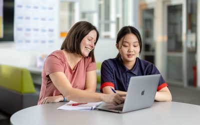 share-image_woodcroft_2022_teacher-with-student-on-laptop_about-us_may2025